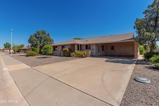 ranch-style home featuring driveway, roof with shingles, an attached carport, and brick siding