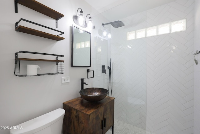 full bathroom featuring a tile shower, vanity, and toilet