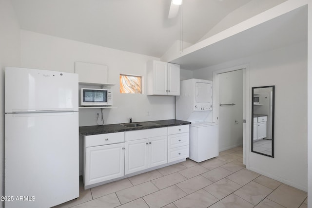 kitchen featuring white appliances, white cabinets, stacked washer / dryer, lofted ceiling, and a sink