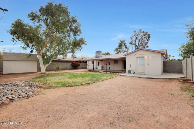 back of house with an outbuilding, a patio, a fenced backyard, a lawn, and a storage unit