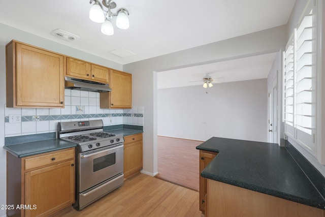 kitchen with visible vents, dark countertops, light wood-style flooring, under cabinet range hood, and stainless steel range with gas cooktop