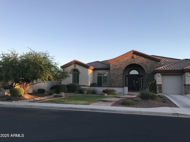 mediterranean / spanish-style home featuring a garage, driveway, stone siding, a tiled roof, and stucco siding