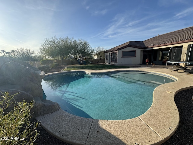 pool with a trampoline, a patio, and fence