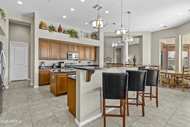 kitchen with brown cabinets, stainless steel appliances, visible vents, an island with sink, and a kitchen bar