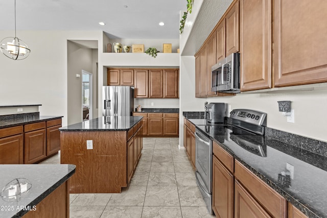 kitchen with dark stone counters, brown cabinetry, appliances with stainless steel finishes, a center island, and hanging light fixtures