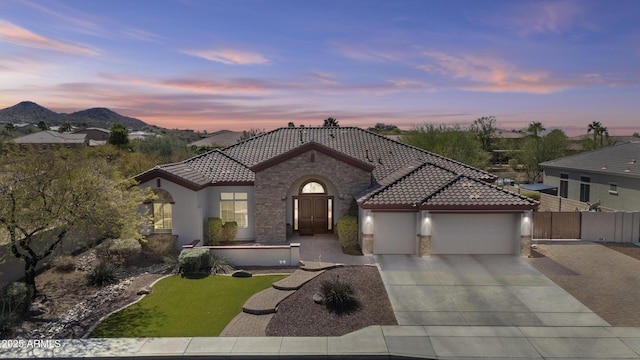 mediterranean / spanish-style home featuring stone siding, an attached garage, a tile roof, and stucco siding