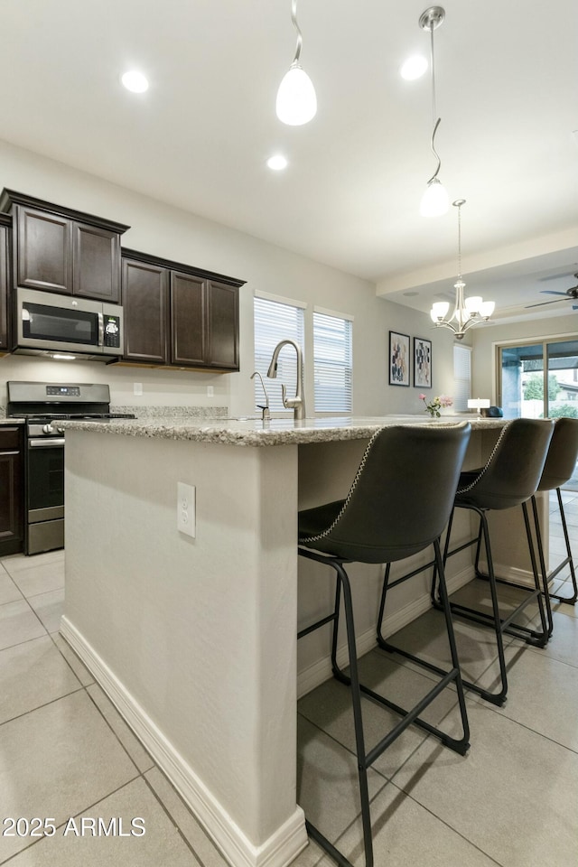 kitchen with a breakfast bar, dark brown cabinets, stainless steel appliances, a kitchen island with sink, and hanging light fixtures