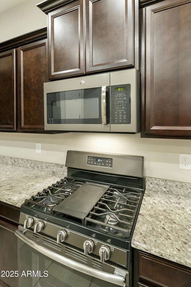 kitchen featuring dark brown cabinetry, light stone counters, and appliances with stainless steel finishes