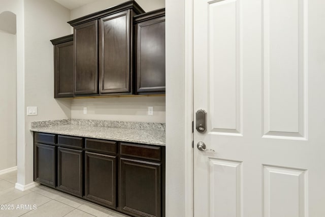 kitchen with light tile patterned floors, dark brown cabinetry, and light stone counters