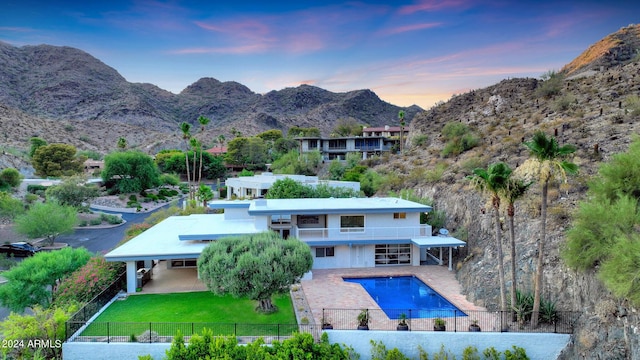 back house at dusk with a lawn, a mountain view, a balcony, and a fenced in pool