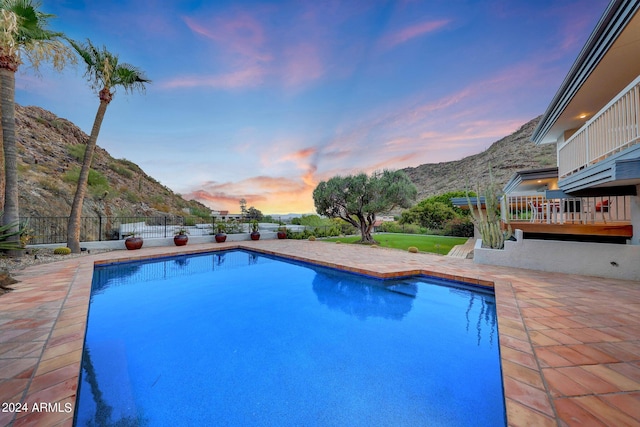 pool at dusk featuring a mountain view and a patio