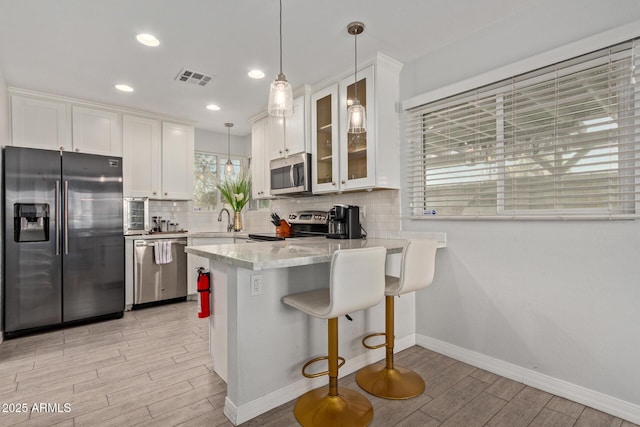 kitchen featuring decorative backsplash, appliances with stainless steel finishes, white cabinets, and decorative light fixtures