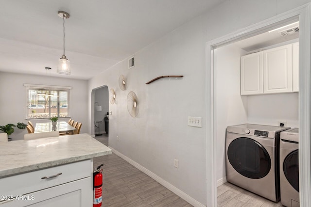 clothes washing area featuring cabinets, washer and dryer, and light hardwood / wood-style flooring