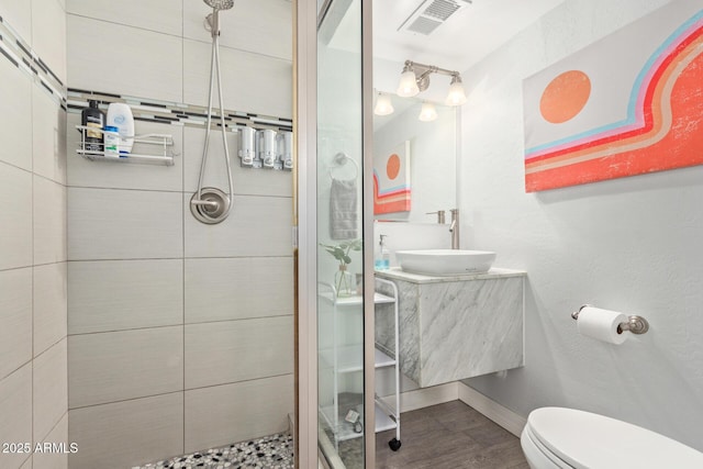 bathroom with hardwood / wood-style flooring, tiled shower, vanity, and toilet