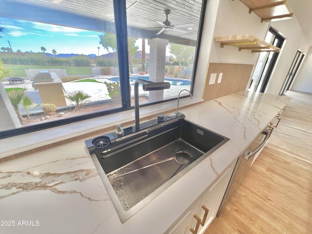 room details with light wood-type flooring, light stone countertops, ceiling fan, and sink