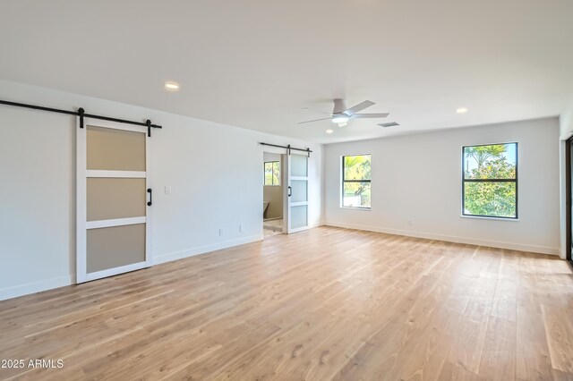 spare room with ceiling fan, a barn door, and light wood-type flooring