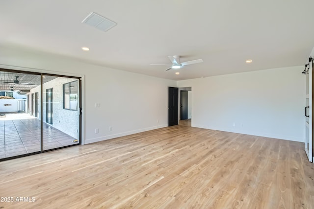 unfurnished room with ceiling fan, a barn door, and light wood-type flooring