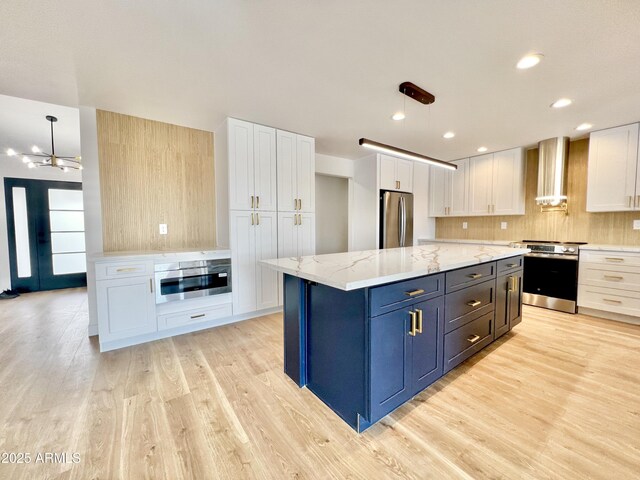 kitchen with appliances with stainless steel finishes, wall chimney range hood, white cabinetry, and pendant lighting