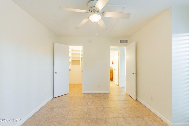 unfurnished bedroom with light tile patterned floors, a closet, ceiling fan, and a spacious closet