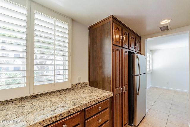 kitchen with stainless steel refrigerator, light tile patterned floors, and light stone countertops