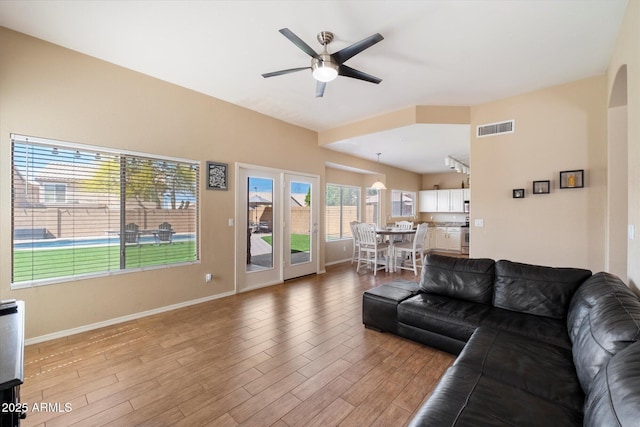 living area featuring baseboards, a ceiling fan, visible vents, and light wood-style flooring