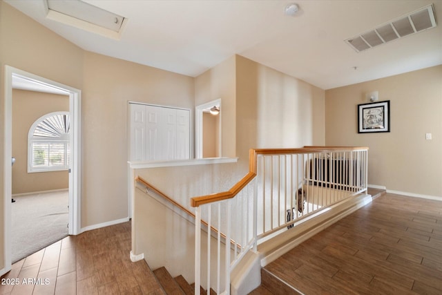 hallway featuring wood finished floors, visible vents, baseboards, and an upstairs landing