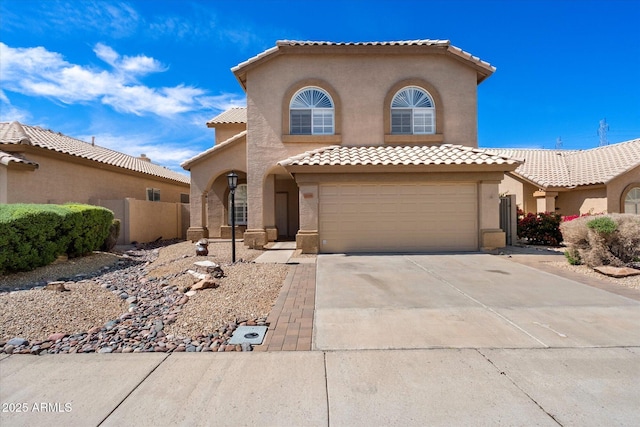 mediterranean / spanish house with concrete driveway, a tiled roof, fence, a garage, and stucco siding