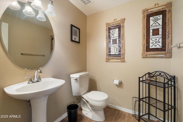 half bath with visible vents, baseboards, wood finished floors, and toilet