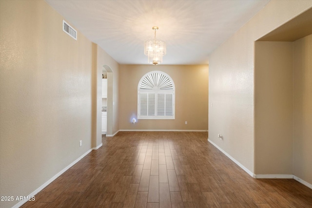 unfurnished dining area with arched walkways, dark wood-style flooring, baseboards, visible vents, and a notable chandelier