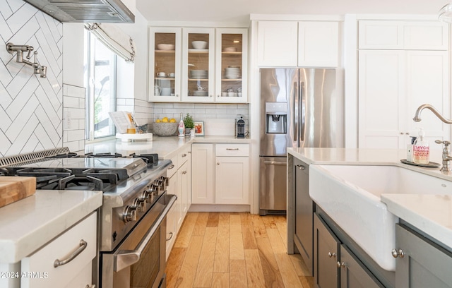 kitchen with tasteful backsplash, white cabinetry, appliances with stainless steel finishes, and light hardwood / wood-style floors