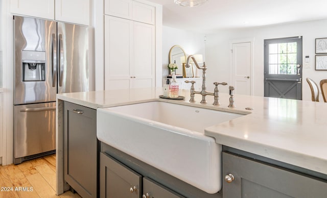 kitchen with stainless steel refrigerator with ice dispenser, sink, gray cabinetry, light wood-type flooring, and white cabinets