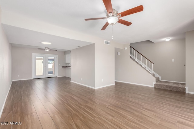 unfurnished living room with stairs, french doors, visible vents, and light wood-style flooring