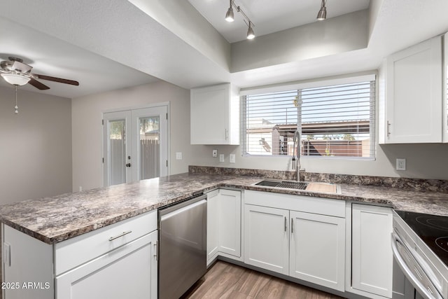 kitchen featuring light wood finished floors, white cabinets, a peninsula, stainless steel appliances, and a sink