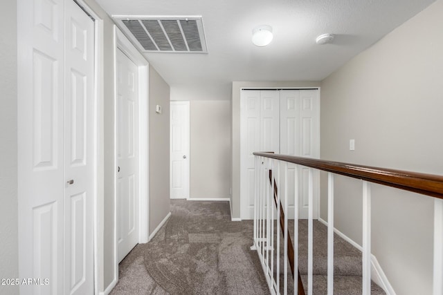 hallway featuring an upstairs landing, carpet flooring, visible vents, and baseboards