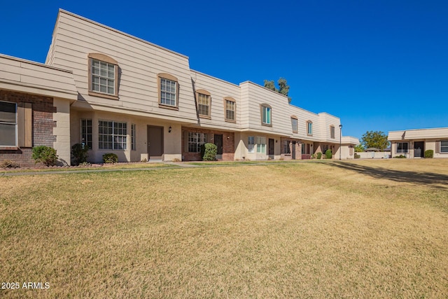 townhome / multi-family property with mansard roof, a front yard, and brick siding