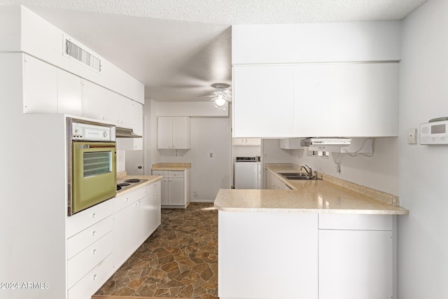 kitchen with wall oven, white cabinetry, sink, and kitchen peninsula