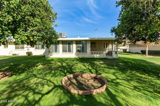 back of house with a sunroom, a yard, and an outdoor fire pit