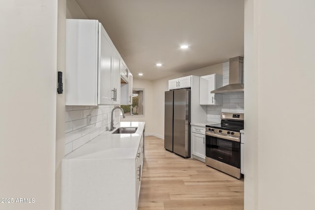 kitchen with appliances with stainless steel finishes, light countertops, a sink, and wall chimney range hood