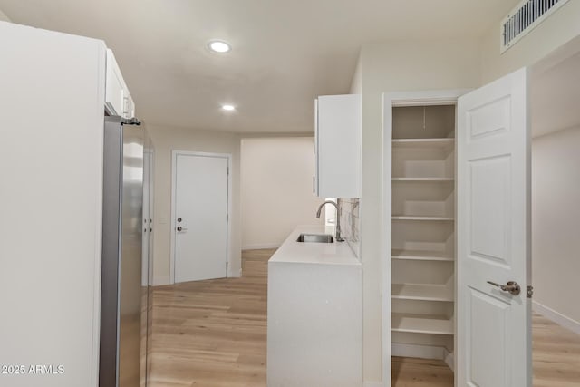 interior space with light wood-style flooring, a sink, visible vents, white cabinets, and freestanding refrigerator