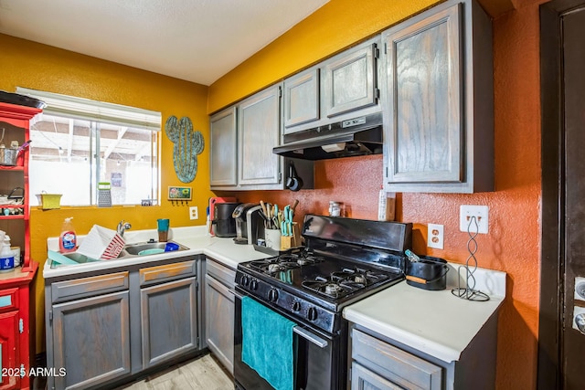 kitchen featuring a textured wall, light countertops, black gas stove, under cabinet range hood, and a sink