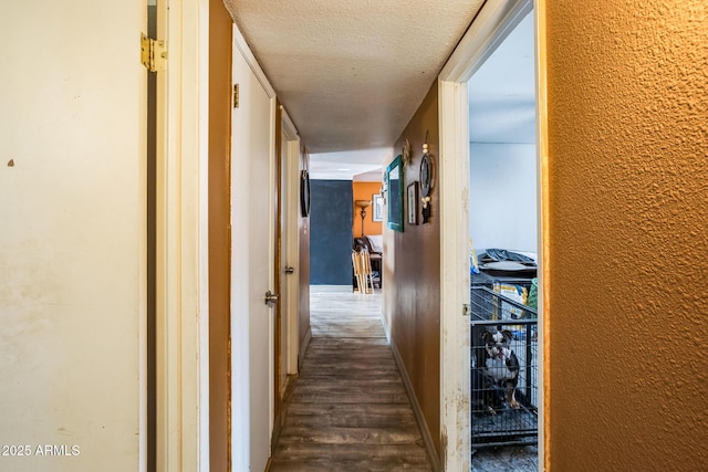 hall with dark wood-type flooring, a textured wall, a textured ceiling, and baseboards