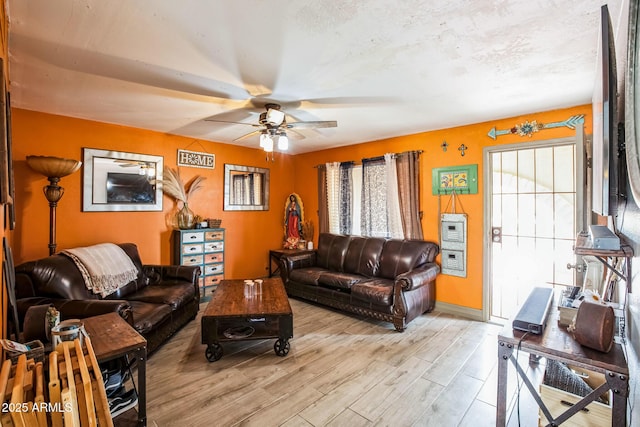 living area with light wood finished floors, ceiling fan, baseboards, and a textured ceiling