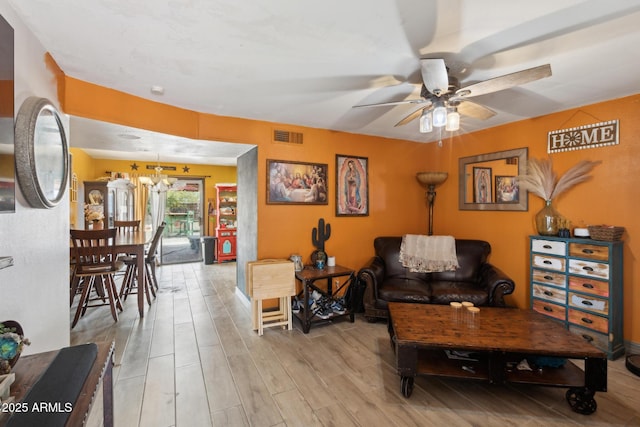 living room with light wood-style flooring, visible vents, and ceiling fan with notable chandelier