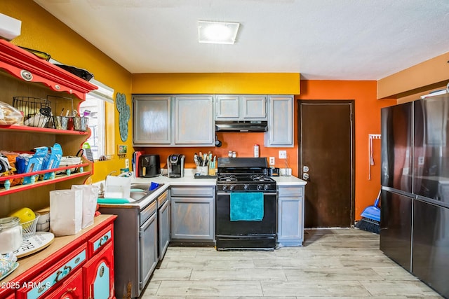 kitchen with light wood-style flooring, under cabinet range hood, light countertops, black appliances, and open shelves