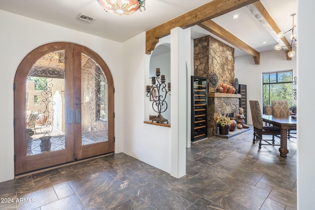 foyer entrance featuring visible vents, beamed ceiling, stone tile flooring, french doors, and a chandelier