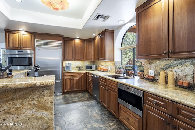 kitchen with a raised ceiling, visible vents, a sink, and built in appliances