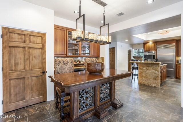 kitchen with stainless steel appliances, visible vents, backsplash, brown cabinetry, and glass insert cabinets