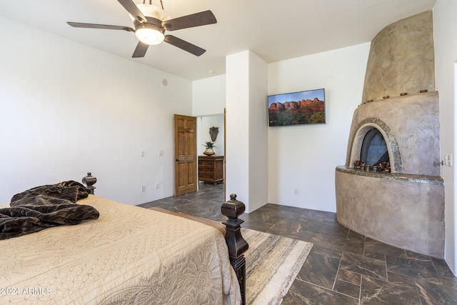 bedroom with a large fireplace, stone finish flooring, and a ceiling fan