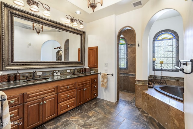 bathroom with double vanity, stone tile floors, visible vents, a garden tub, and a sink