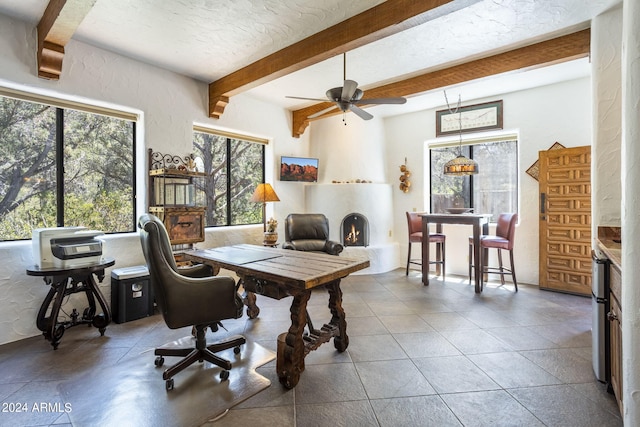 home office featuring a textured ceiling, a textured wall, a fireplace, a ceiling fan, and beam ceiling